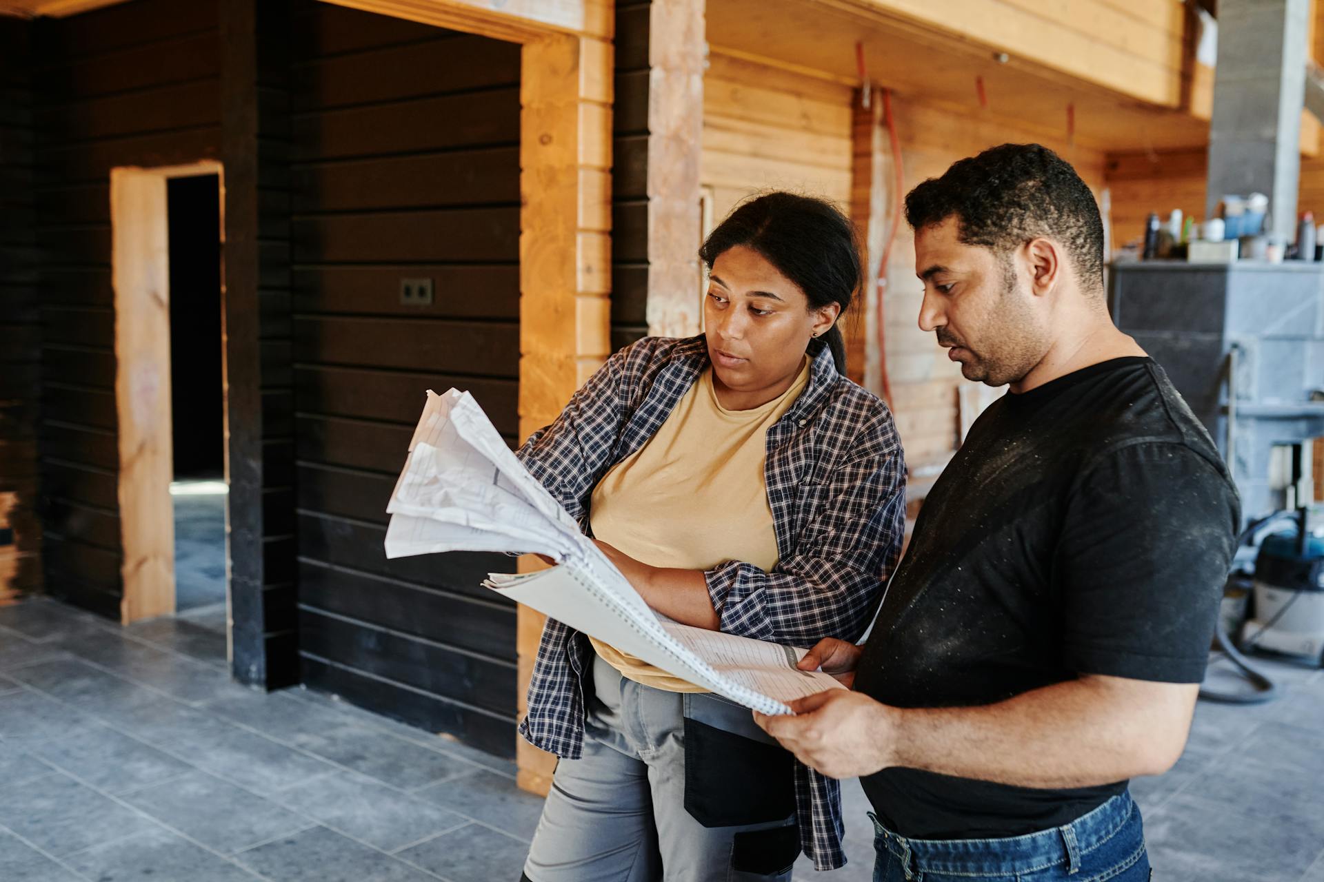 Two remodeling contractors reviewing construction plans inside a partially-finished home